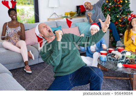 Image of happy caucasian man singing karaoke celebrating christmas at home with diverse friends Image of happy caucasian man singing karaoke celebrating christmas at home with diverse friends 95649084