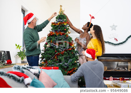Image of happy diverse friends celebrating christmas at home decorating the tree Image of happy diverse friends celebrating christmas at home decorating the tree 95649086