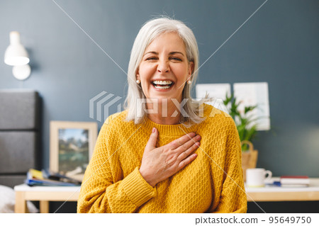 Happy caucasian senior woman making video call at home smiling to camera and touching chest Happy caucasian senior woman making video call at home smiling to camera and touching chest 95649750
