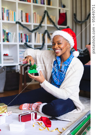 Happy african american woman wearing santa claus hat, packing presents Happy african american woman wearing santa claus hat, packing presents 95649751