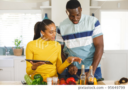 Happy diverse couple using recipe on tablet preparing food together in kitchen 95649799