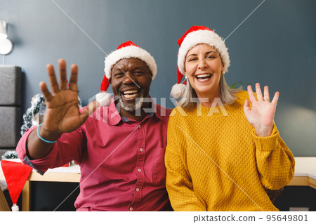 Happy diverse senior couple in santa hats making christmas video call waving to camera 95649801