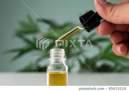 Legalized cannabis sativa hemp leaf and container of CBD oil with dropper lid. 95652019