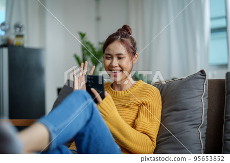 portrait of a young Asian woman woman holding smartphone while sitting on sofa. 95653852