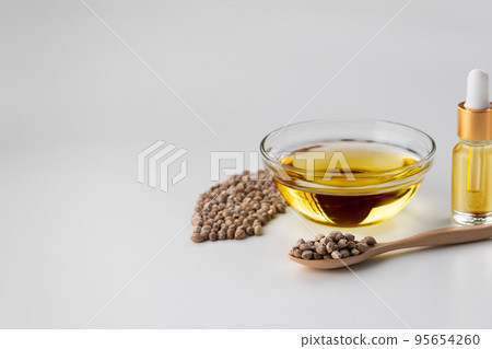 Pile of hemp seed on wooden spoon with legalized CBD oil on clear glass bowl 95654260