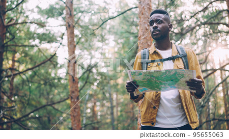 African American man is walking in forest looking at paper map searching for desired tourist destination . Nature, active lifestyle and navigation concept. 95655063