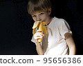 young boy is eating banana on black background. Diet and fruits. 95656386
