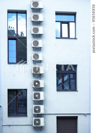 Vertical row of air condicioners on white building with asymmetrical windows with blue sky reflection in windows glass 95656956