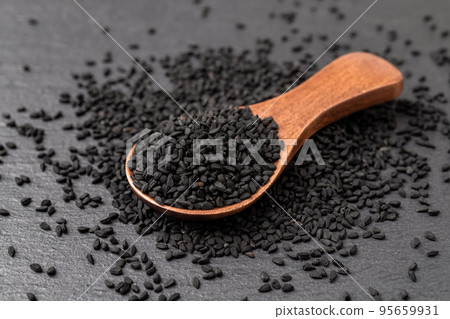 Black cumin seeds in a wooden spoon over black background. Black cumin seeds in a wooden spoon over black background. 95659931