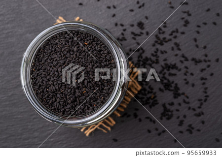 Glass jar full of black cumin seeds over black background. 95659933