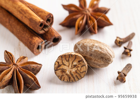 Whole and halved nutmeg seeds, cinnamon sticks, few cloves, and star anise on a wooden background. Whole and halved nutmeg seeds, cinnamon sticks, few cloves, and star anise on a wooden background. 95659938