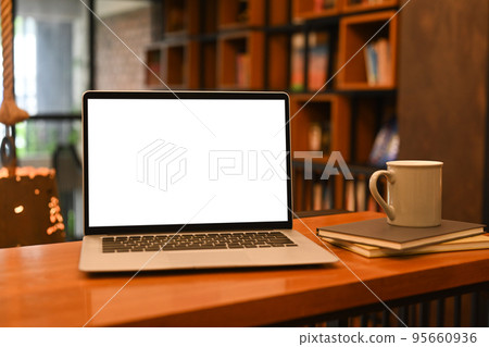 Mock up laptop computer, books and coffee cup on wooden table against blurred bookshelf background Mock up laptop computer, books and coffee cup on wooden table against blurred bookshelf background 95660936