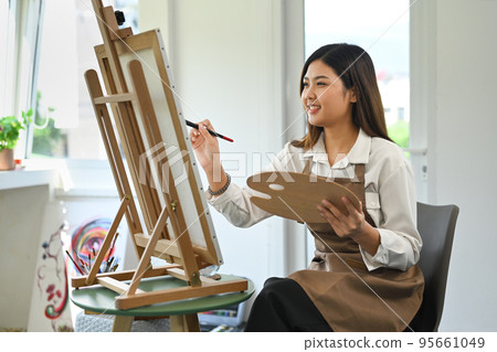 Pleasant woman painting picture on easel at bright home studio. Leisure activity, creative hobby and art concept 95661049