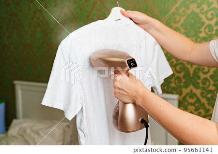 woman irons white t-shirt by portable hand steamer for clothes. 95661141
