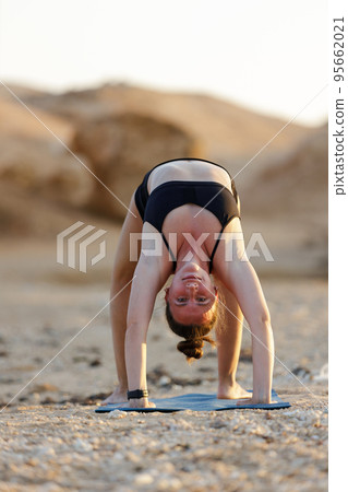 Young woman doing wheel yoga pose at the beach in the evening Young woman doing wheel yoga pose at the beach in the evening 95662021