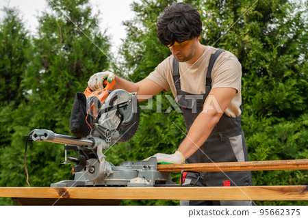 Man using a modern electric circular saw in a backyard workshop 95662375