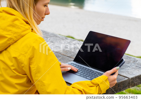 An inspiring woman smiles and scrolls the screen of her smartphone and uses social media on laptop 95663403