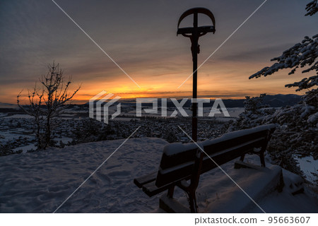 Empty lonely bench and cross with Jesus Christ in cold snowy winter morning in village Martincek, Slovakia Empty lonely bench and cross with Jesus Christ in cold snowy winter morning in village Martincek, Slovakia 95663607