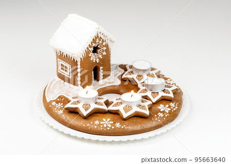 Advent candlestick with two lighted candles and christmas homemade gingerbread house on white background Advent candlestick with two lighted candles and christmas homemade gingerbread house on white background 95663640