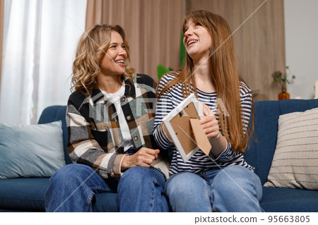 Adult daughter and her mature mother looking at photo in frame while sitting on the sofa in home. Family, generation and people concept Adult daughter and her mature mother looking at photo in frame while sitting on the sofa in home. Family, generation and people concept 95663805