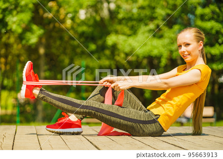 Girl doing exercise outdoor, using resistance fit band. 95663913