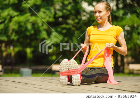 Girl doing exercises outdoor, using resistance fit band. 95663924