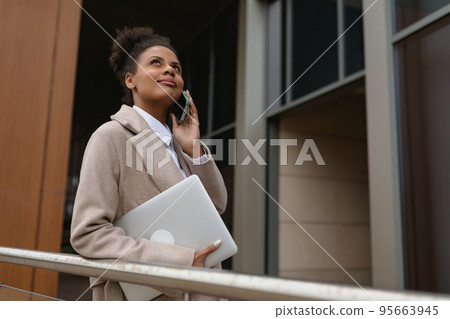 Business african american woman with a laptop in her hands speaks on a mobile phone next to an 95663945