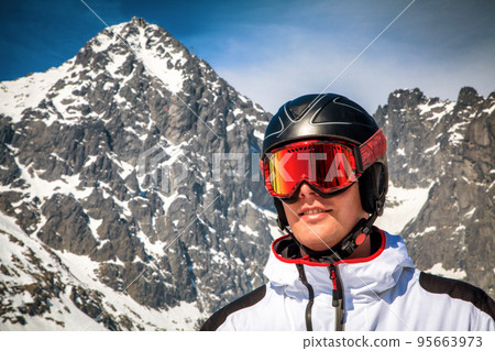 Male skier with ski goggles and helmet and snowy peak at background 95663973
