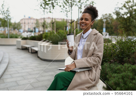 portrait african american smiling woman with laptop and cup of coffee outside office, concept of portrait african american smiling woman with laptop and cup of coffee outside office, concept of 95664101