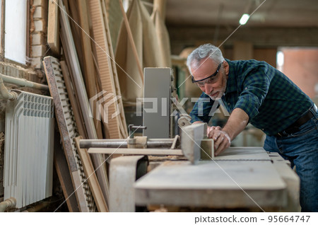 Mature carpenter working in a workshop and looking involved Mature carpenter working in a workshop and looking involved 95664747