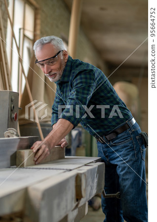 Mature carpenter working in a worshop and looking involved Mature carpenter working in a worshop and looking involved 95664752