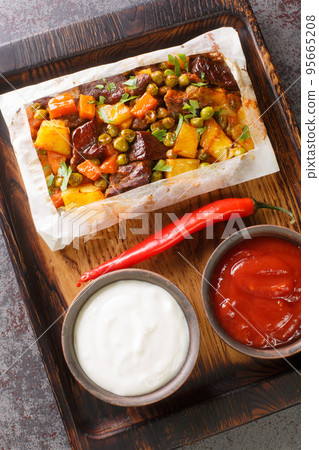 Kagit Kebabi wrapped meat with favorite vegetables in greaseproof paper and baked close-up on a wooden tray. Vertical top view Kagit Kebabi wrapped meat with favorite vegetables in greaseproof paper and baked close-up on a wooden tray. Vertical top view 95665208