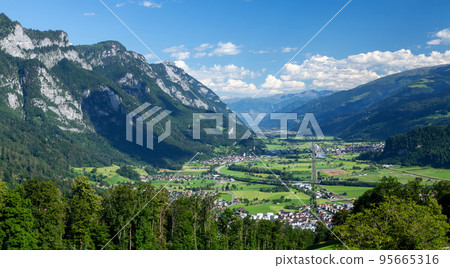 Panoramic view of countryside, green alpine meadows and mountains Panoramic view of countryside, green alpine meadows and mountains 95665316