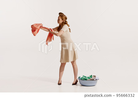 Portrait of young elegant woman washing clothes isolated over white background. Squeezing water 95666332