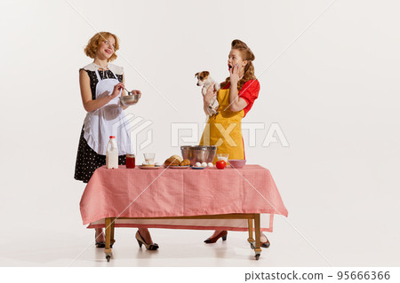 Portrait of two elegant, stylish women doing cooking together and discussing rumors isolated over white background 95666366