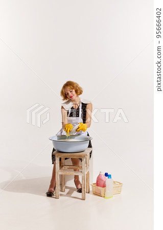 Portrait of stylish woman in dress and apron washing the dishes in foamy bowl isolated on white background 95666402