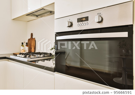 Fragment of interior of light narrow home kitchen with minimalist style white furniture with sink and stove Fragment of interior of light narrow home kitchen with minimalist style white furniture with sink and stove 95666591