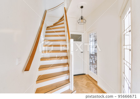 White spiral stairway connecting levels of contemporary house with wooden floor and white walls 95666671