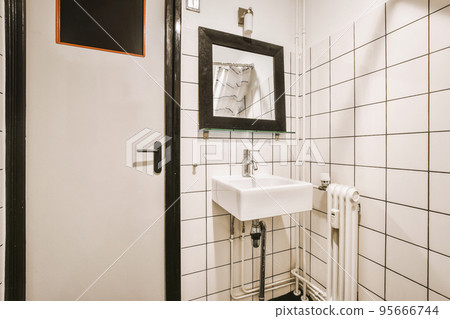 Modern flush toilet and ceramic sink installed on white tiled walls near mirror and towel in small restroom at home Modern flush toilet and ceramic sink installed on white tiled walls near mirror and towel in small restroom at home 95666744