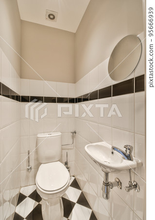 Interior of narrow restroom with sink and wall hung toilet with white walls and checkered floor Interior of narrow restroom with sink and wall hung toilet with white walls and checkered floor 95666939
