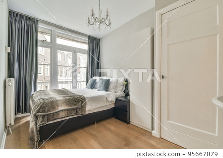 Bed with colorful pillows and blanket located near glass wall of restroom in modern apartment 95667079