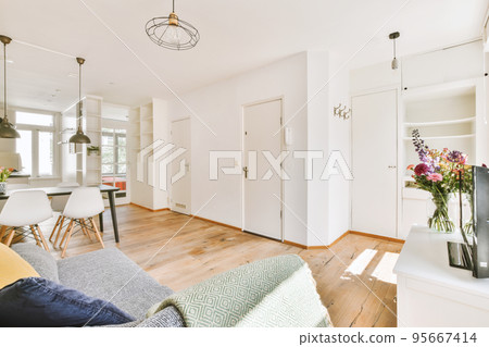 Shabby wooden table with chairs and vase located near comfortable couch against light walls with decorations and TV in modern apartment 95667414