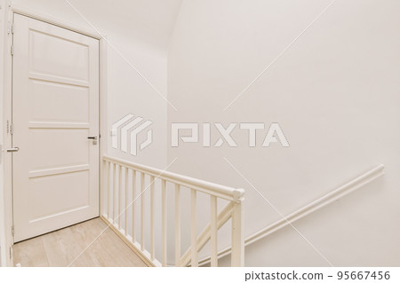 Closed white door of room located near framed pictures and stylish lamp on top of stairway at home Closed white door of room located near framed pictures and stylish lamp on top of stairway at home 95667456