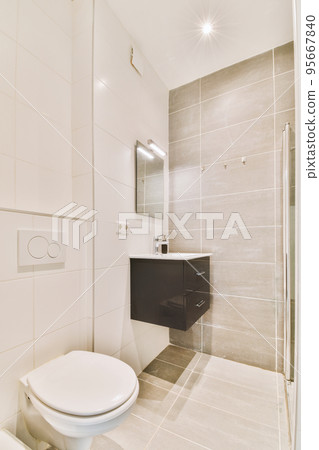 Modern flush toilet and ceramic sink installed on white tiled walls near mirror and towel in small restroom at home 95667840
