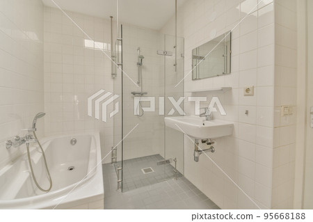 Sinks with mirrors and clean bathtub located near shower box with glass door in modern bathroom with white tiled walls 95668188