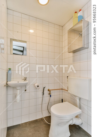 Interior of narrow restroom with sink and wall hung toilet with white walls and checkered floor Interior of narrow restroom with sink and wall hung toilet with white walls and checkered floor 95668323