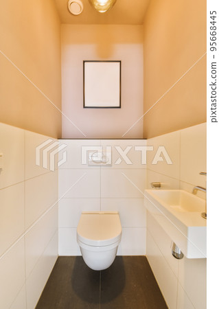 Interior of narrow restroom with sink and wall hung toilet with white walls and checkered floor Interior of narrow restroom with sink and wall hung toilet with white walls and checkered floor 95668445