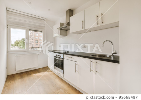 Fragment of interior of light narrow home kitchen with minimalist style white furniture with sink and stove Fragment of interior of light narrow home kitchen with minimalist style white furniture with sink and stove 95668487