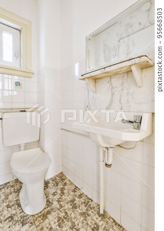 Wall hung toilet and small sink in corner in lavatory room with beige tile Wall hung toilet and small sink in corner in lavatory room with beige tile 95668503