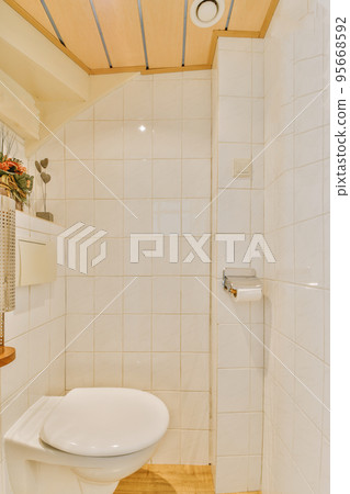 Interior of narrow restroom with sink and wall hung toilet with white walls and checkered floor 95668592